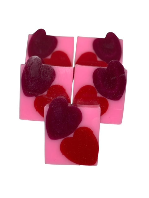 Handmade bar soap with pink base and heart-shaped inclusions, with a purple heart-shaped object on top.
